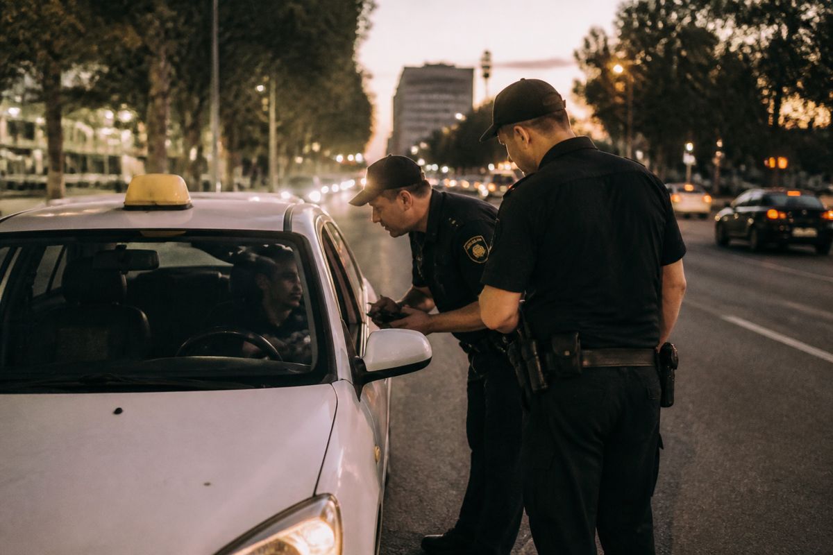 Police officers inspecting a white taxi on a city street at dusk