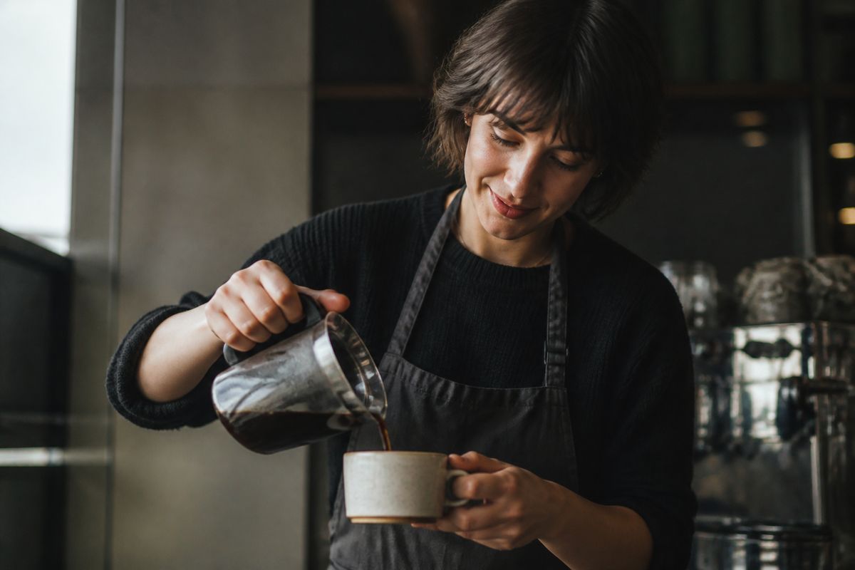 A barista pouring freshly brewed coffee into a cup.