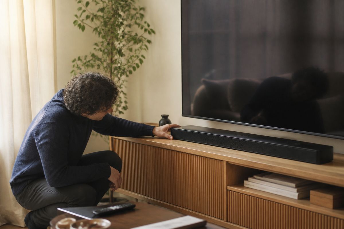 A person adjusting a Bose soundbar in a cozy living room.