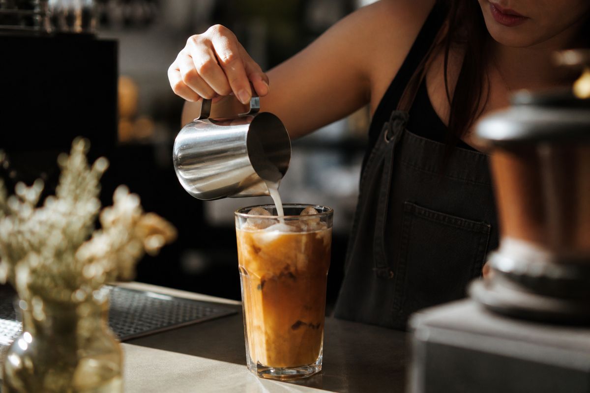 A barista pouring cream into an iced pumpkin latte