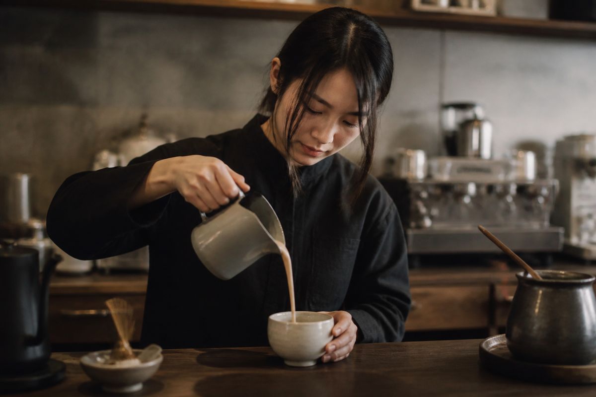 A barista pouring creamy hojicha tea in a cozy café.