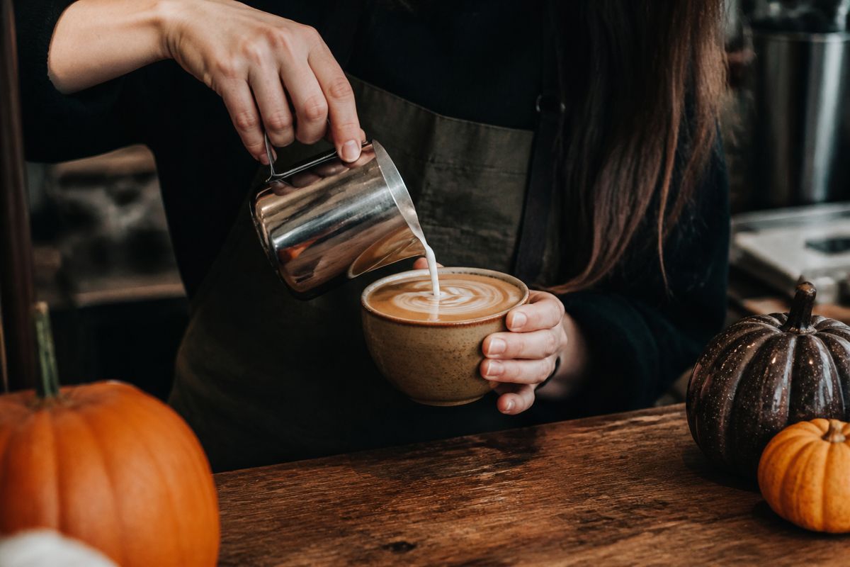 Barista pouring latte art on a pumpkin spice coffee drink