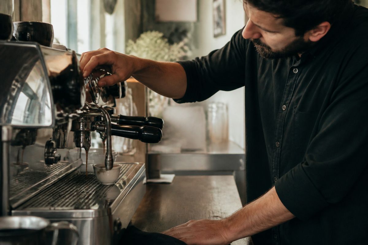 A barista pouring espresso shot from a traditional Italian machine