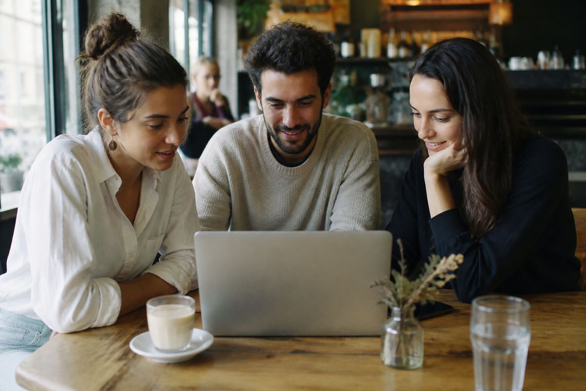 Entrepreneurs collaborating around a laptop in a coffee shop.