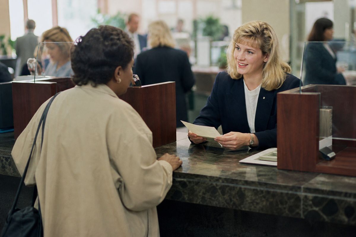 A bank teller assisting a customer at a busy branch counter