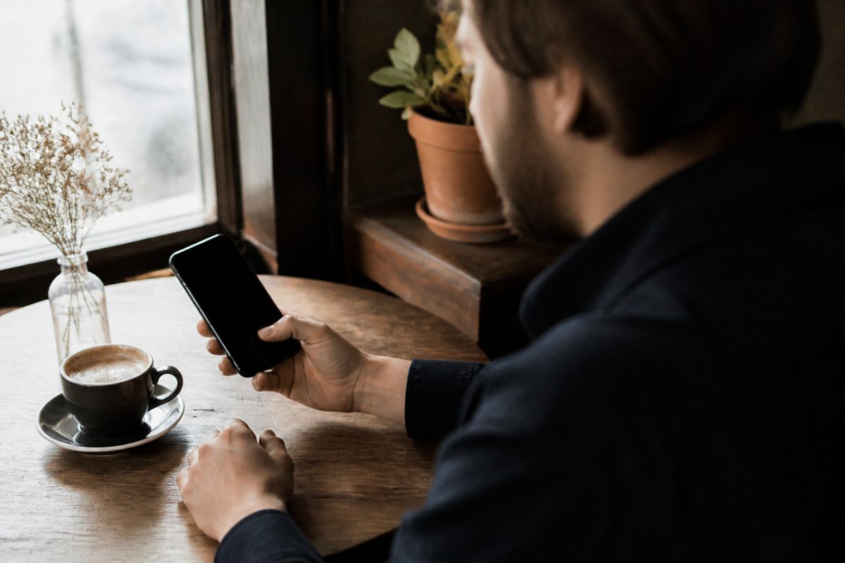 A person checking their savings account on a smartphone at a café table