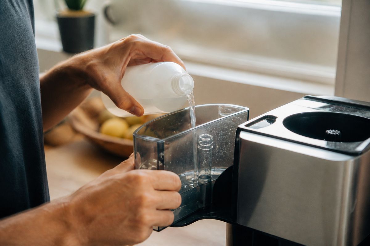 A person pouring descaling solution into a coffee maker reservoir