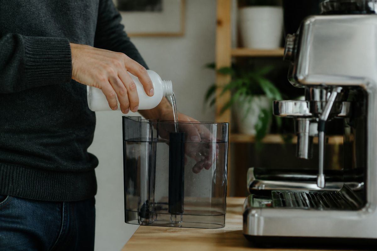 A person pouring descaling solution into a coffee machine reservoir