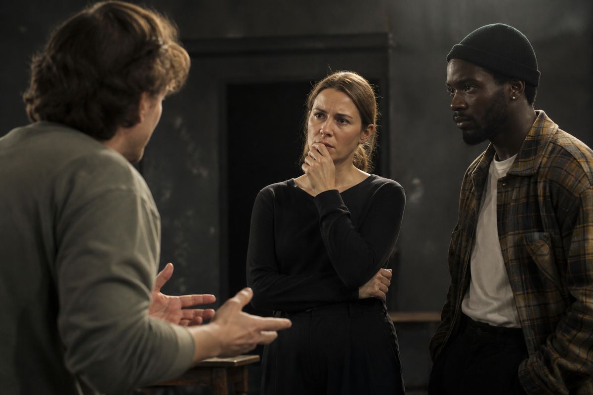 Three actors rehearsing intense dialogue on a dimly lit set