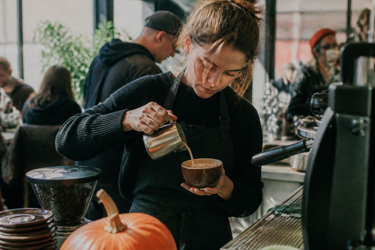Barista pouring a Pumpkin Spice Latte in a busy café