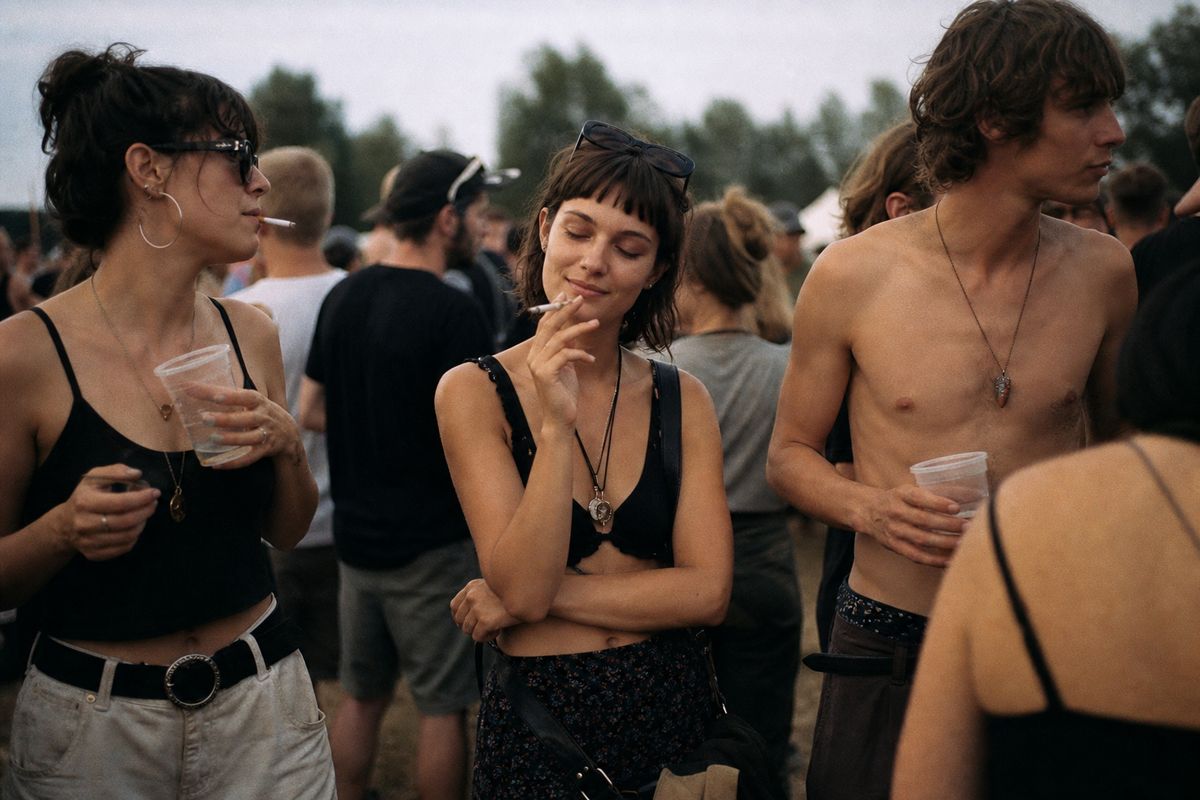 People gathered at a music festival, some holding drinks and smoking.