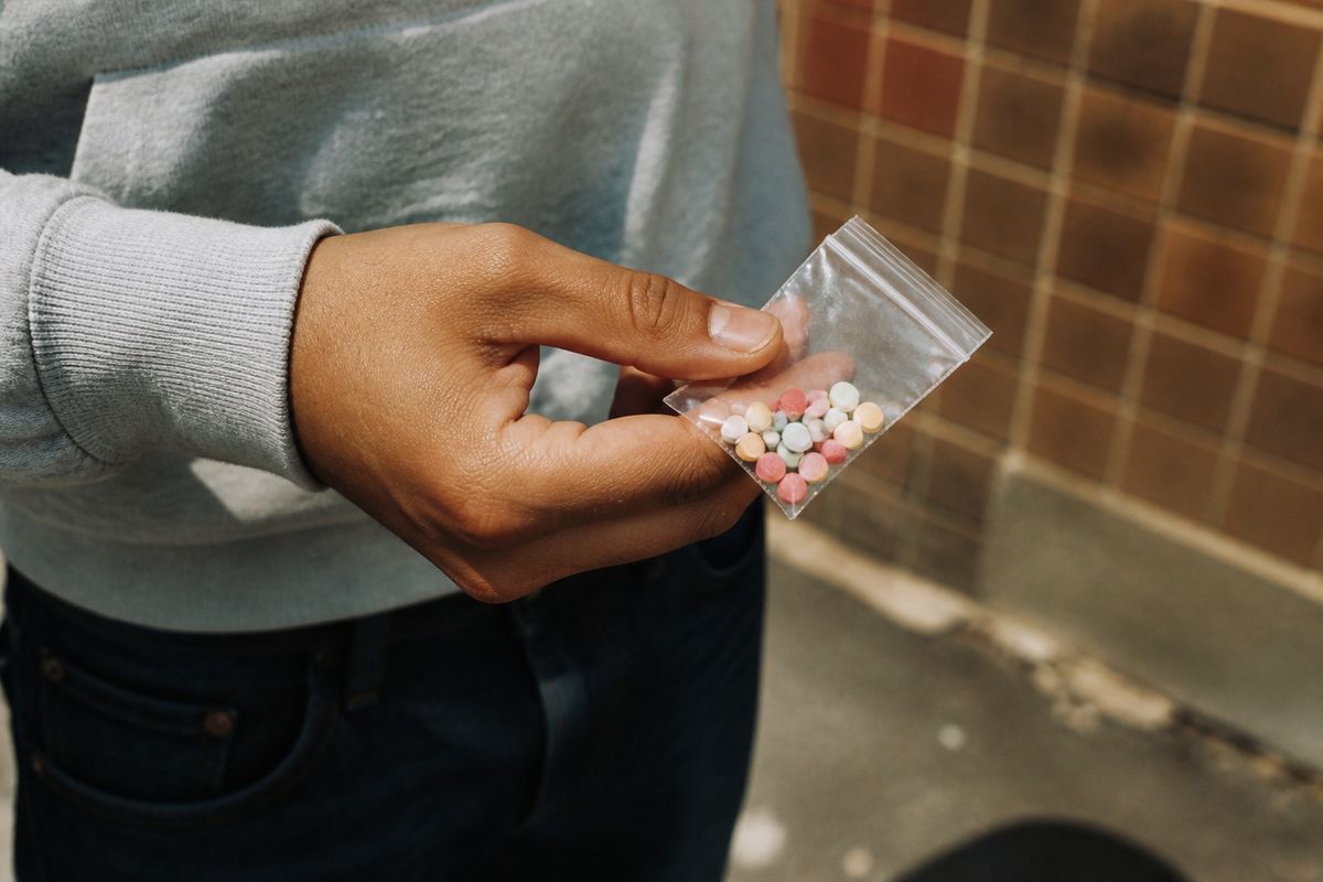 A person holding a small bag of colorful pills outdoors
