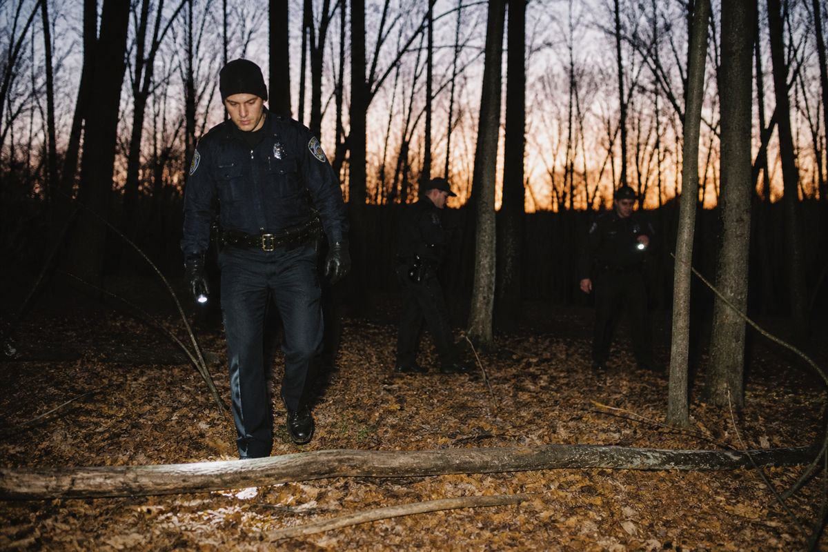Police officers searching a wooded area at dusk